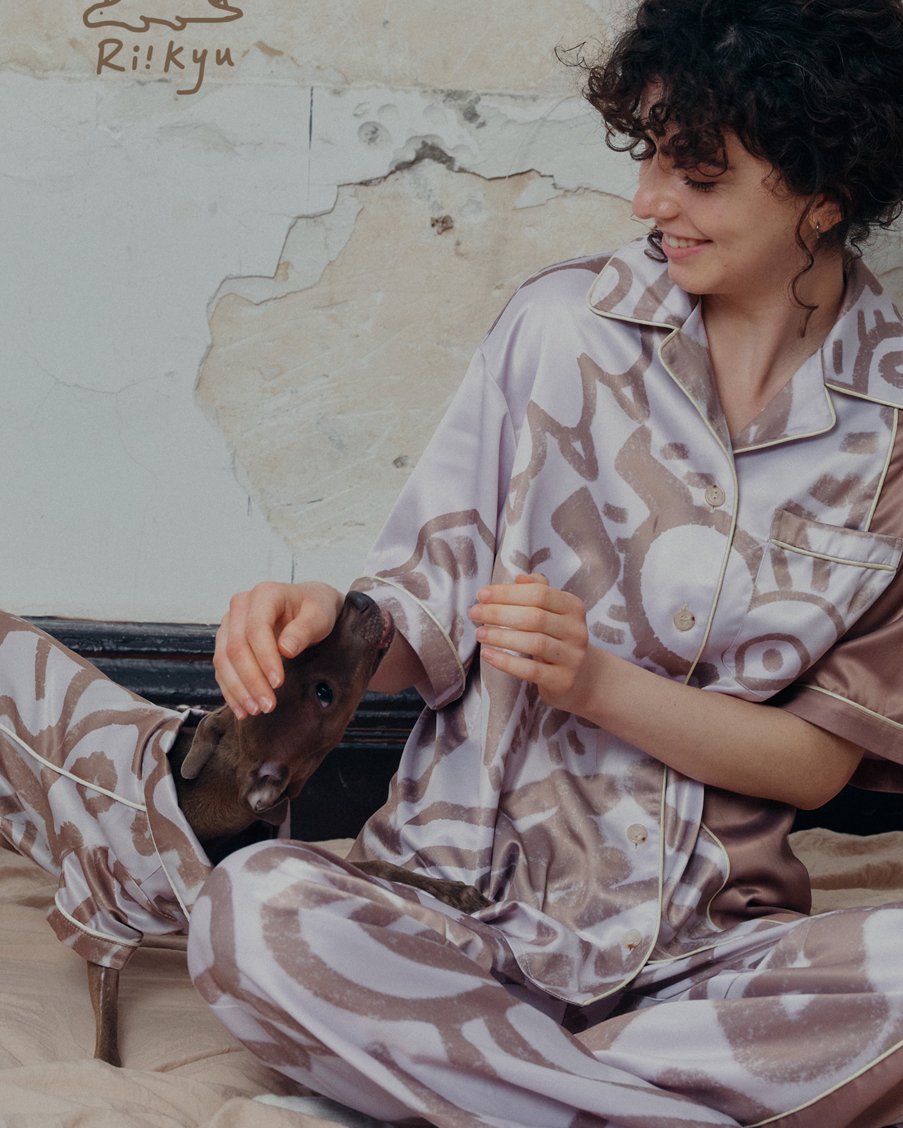 A female model pets a dog's head, both of them wear short sleeve pajama sets.
