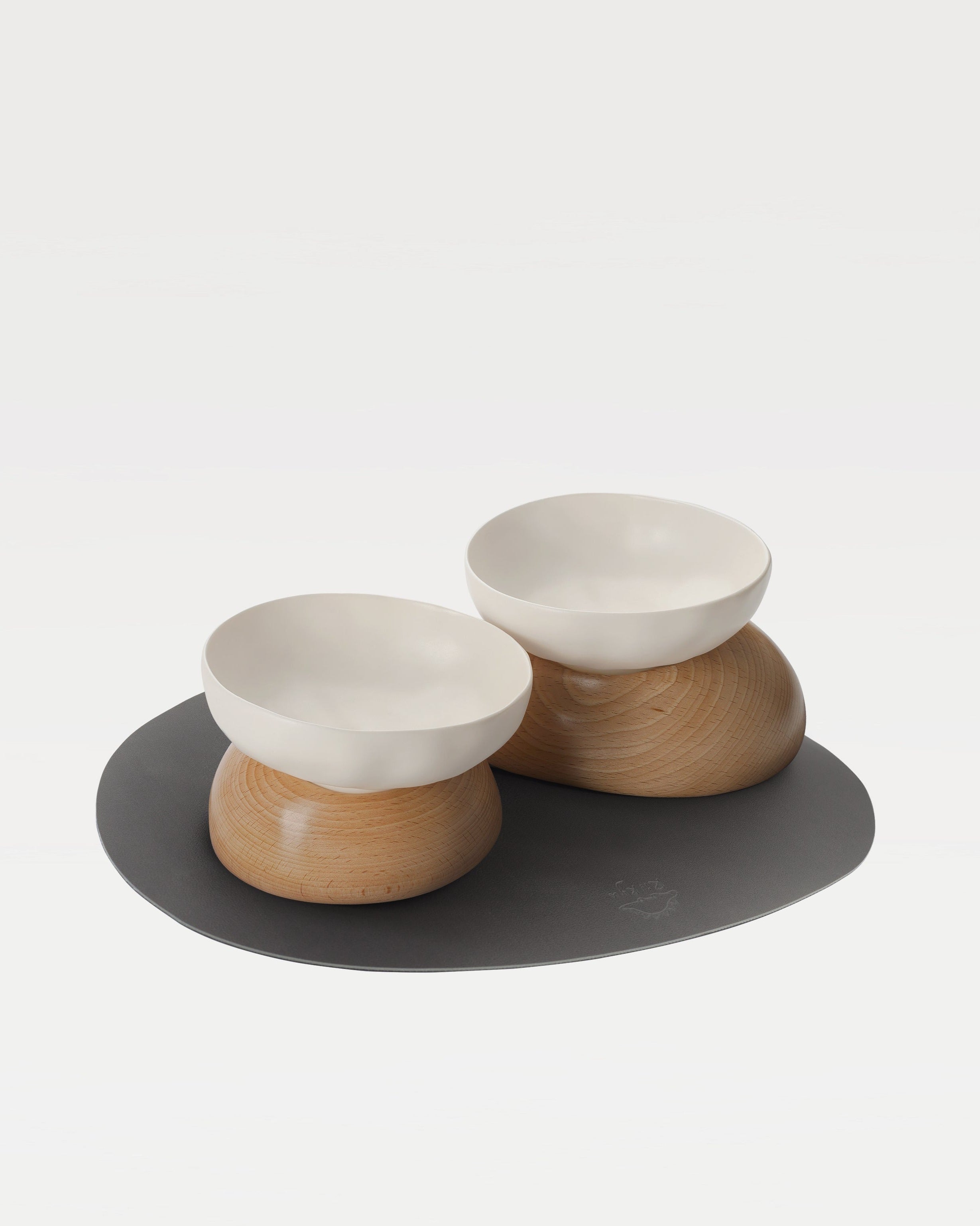 two white bowls, two wooden bases and a black mat
