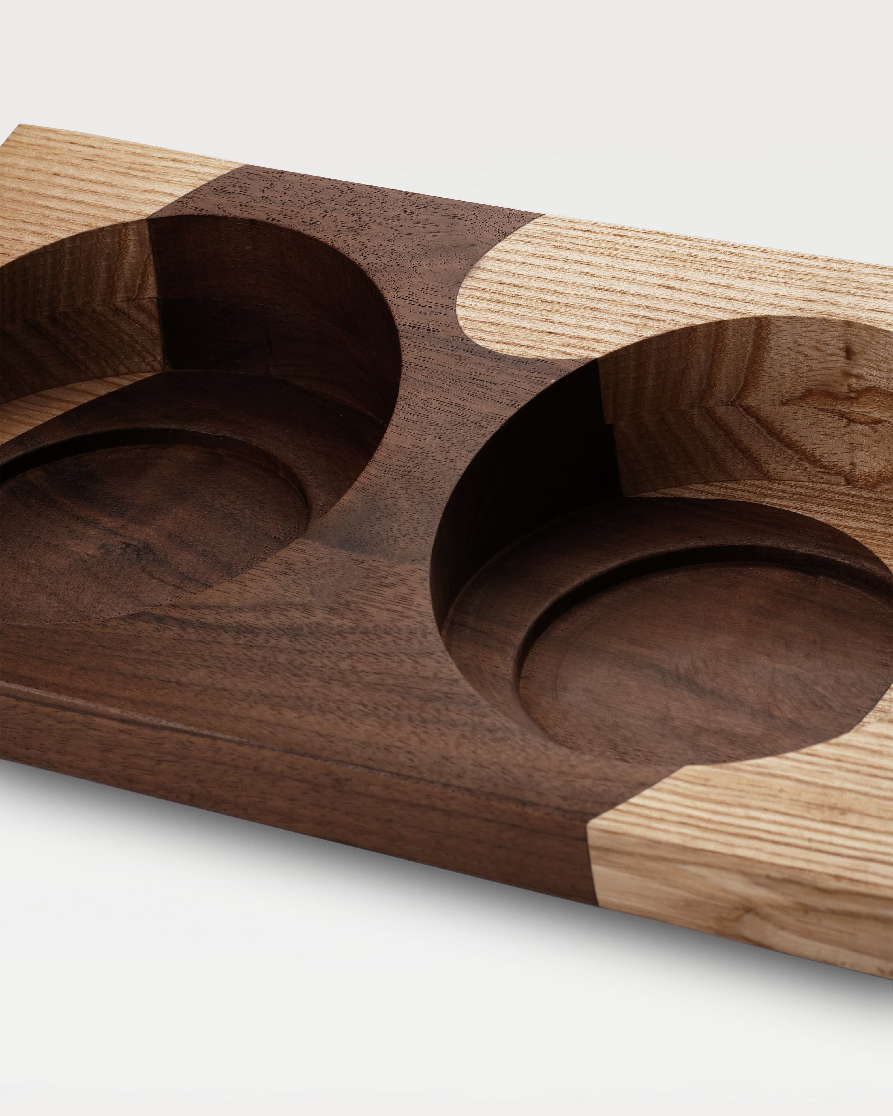 A two-tone wooden trapezoidal base with two grooves for holding bowls