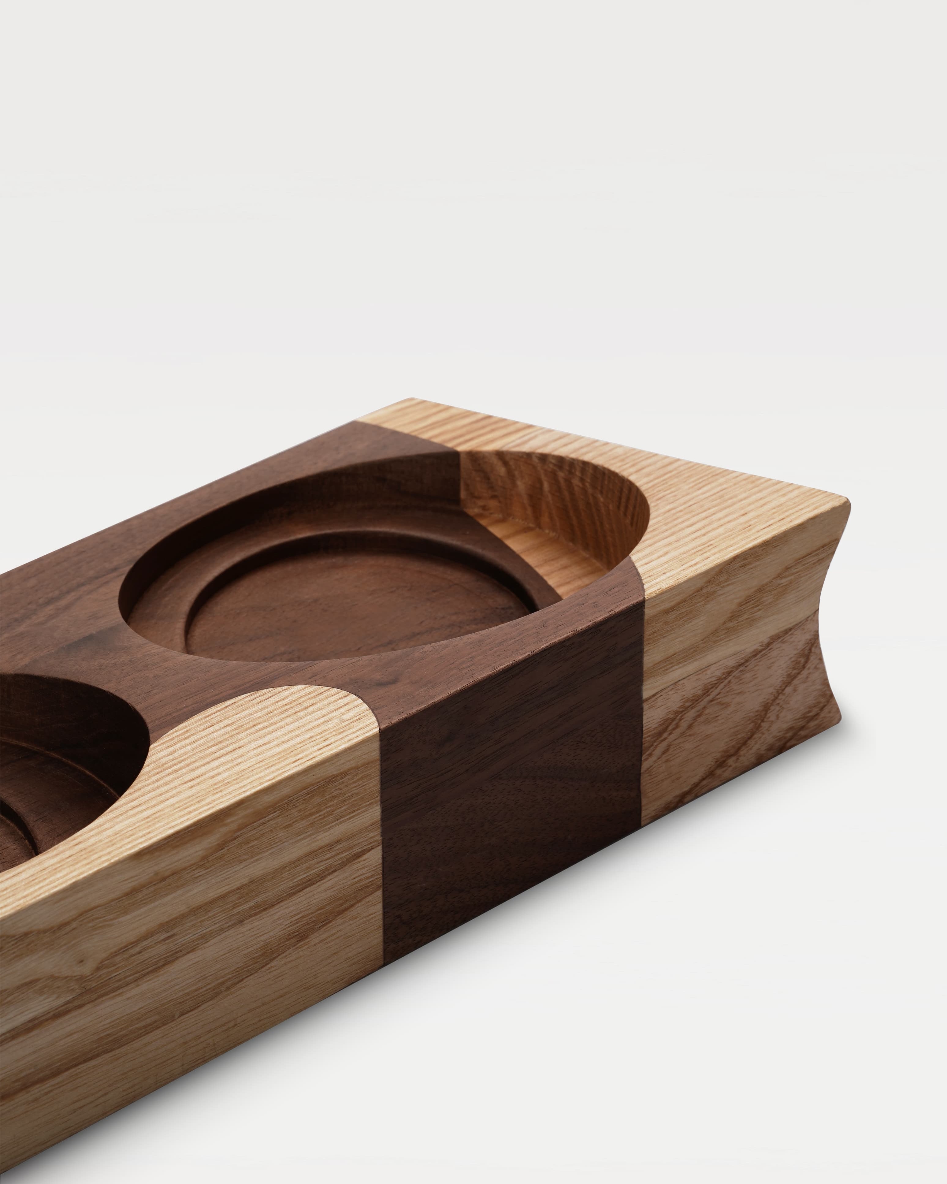 A two-tone wooden trapezoidal base with two grooves for holding bowls