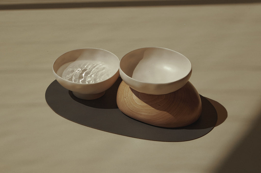 Two pebble bowls, one filled with water and the other with a wooden base underneath, all of which is placed on a black mat