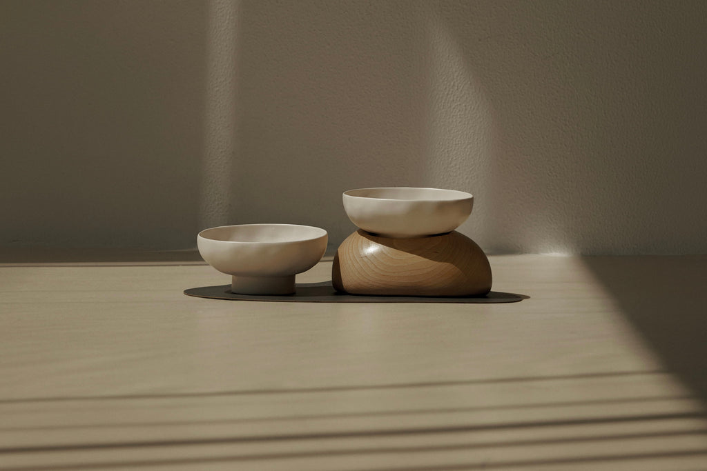 Two pebble bowls, one with a base, placed on a black mat