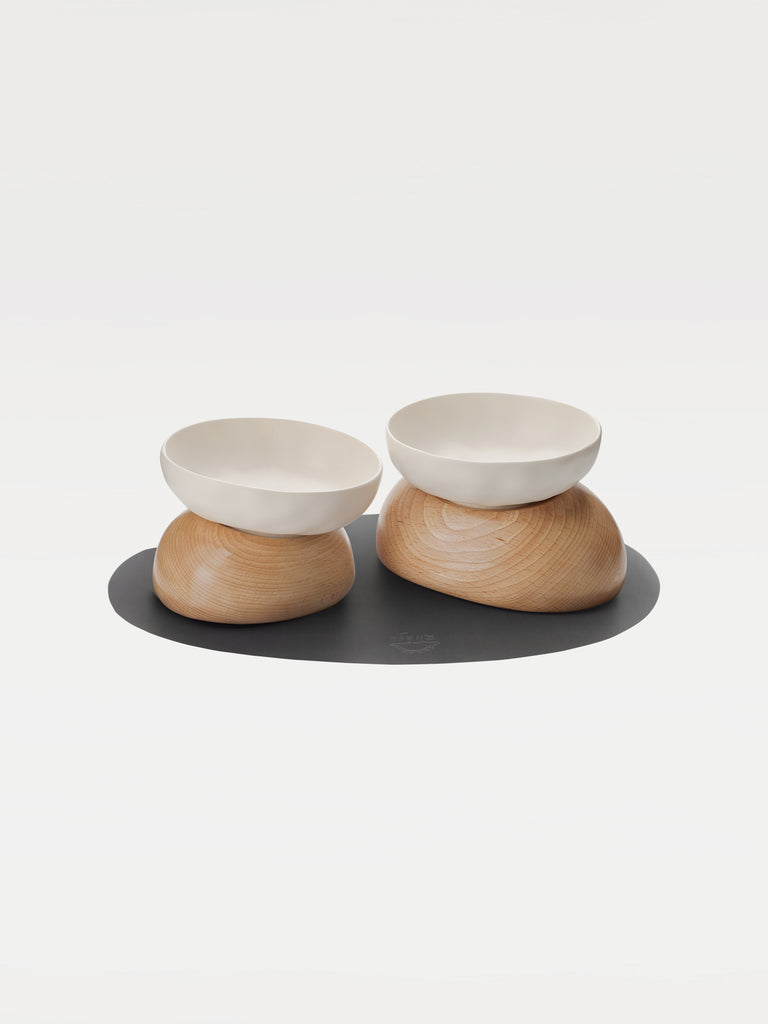 two white bowls, two wooden bases and a black mat