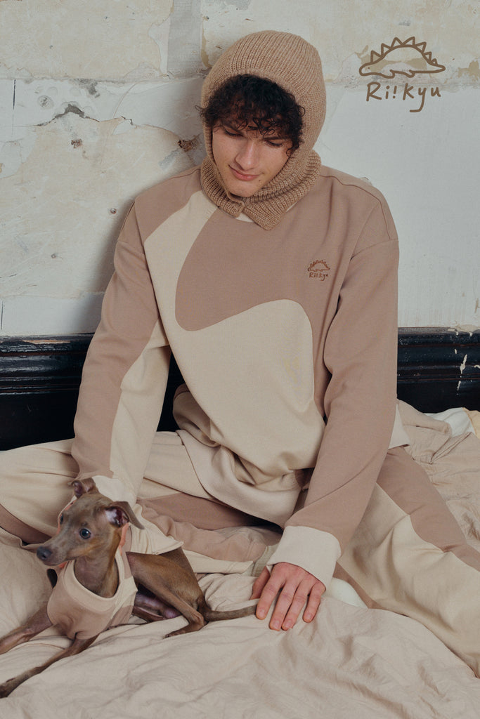 A male model pets a dog, both of them wear patchwork sweatshirt sets.