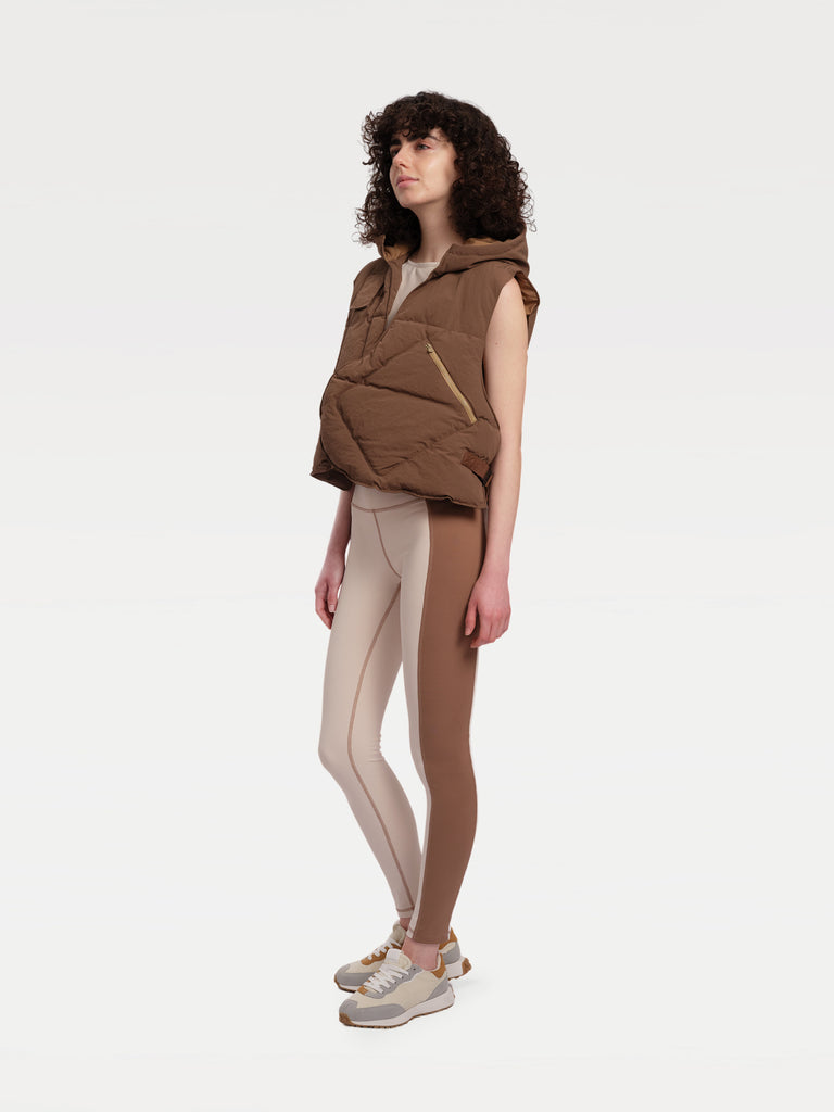 A female model standing sideways in a brown paded vest